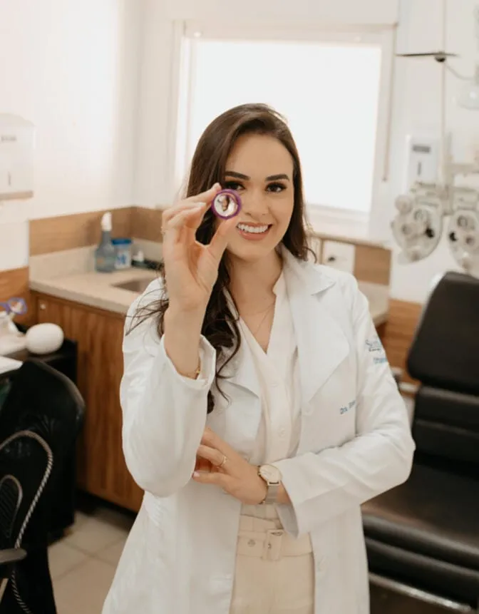 Dra. Bruna Pevide segurando uma lente intraocular na altura do olho